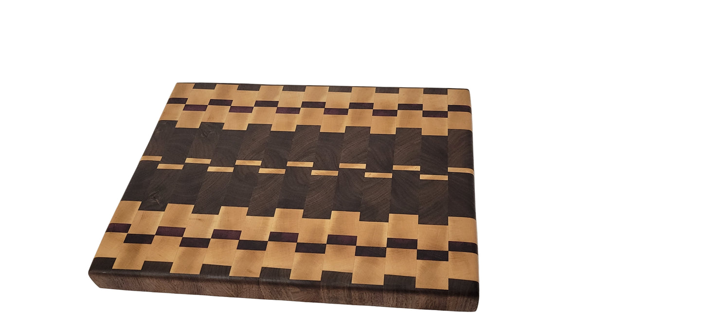 An end grain charcuterie board made from maple, purple heart, and black walnut, featuring a geometric pattern of different wood shades.