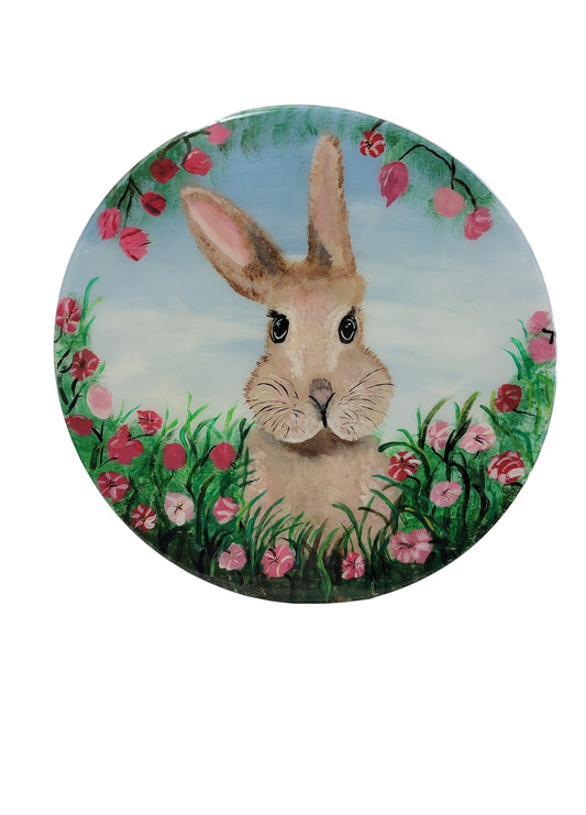 A round birch wood wall art featuring a brown bunny with pink and red floral accents in the background.