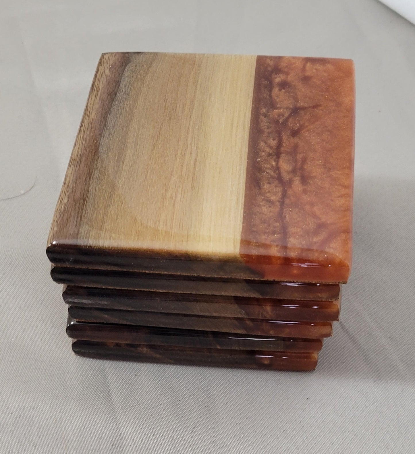 A stack of four square coasters made of black walnut wood with copper epoxy resin rivers, with a clear resin finish and cork backing.