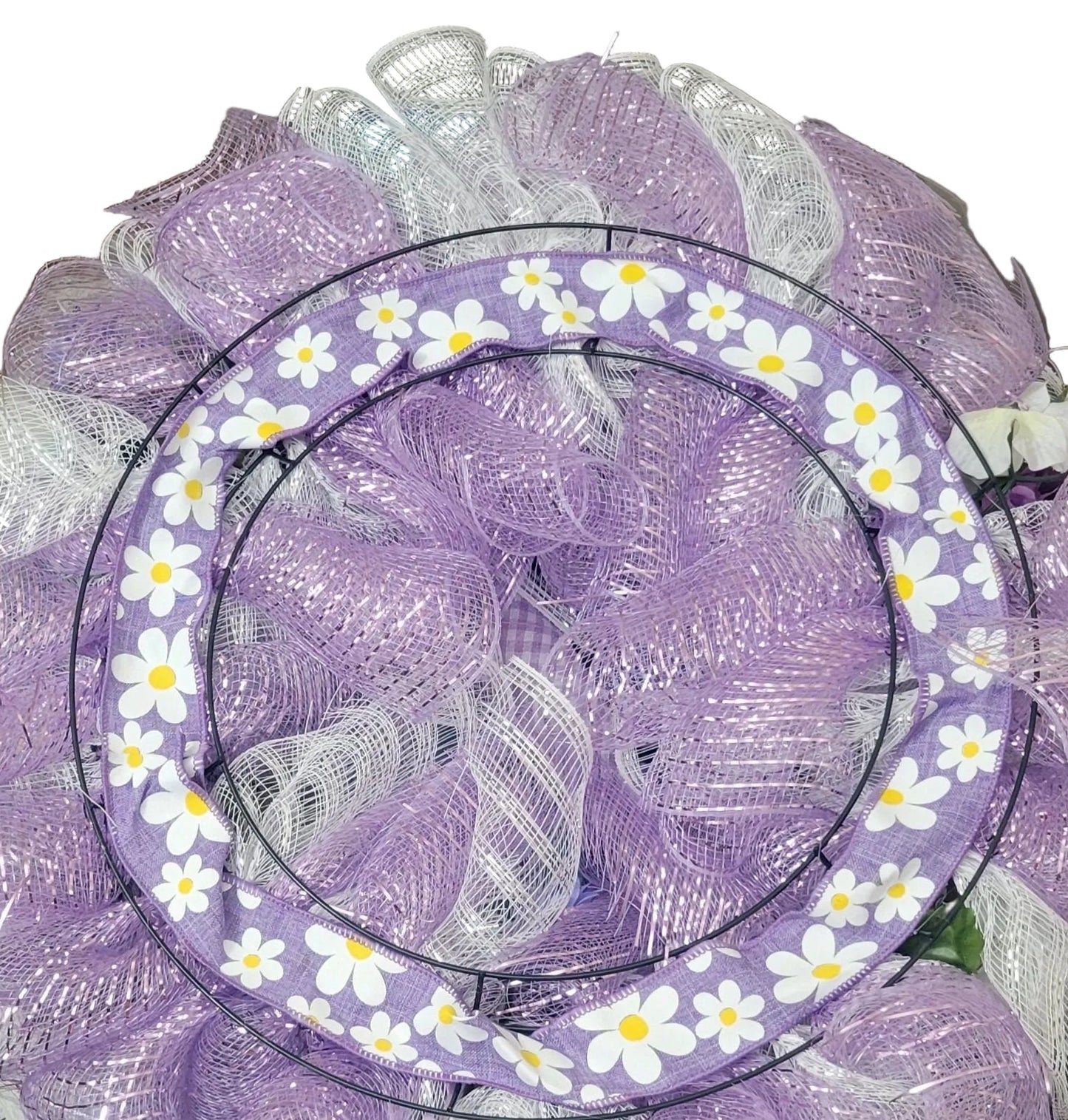 Decorative wreath with purple mesh and white flowers on a table.