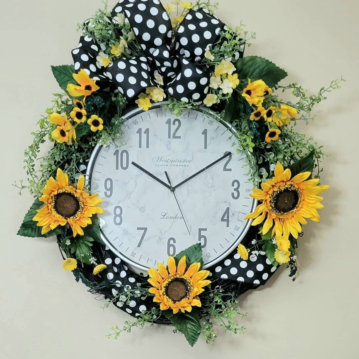 Decorative wall clock with sunflowers and a polka dot bow on a plain background