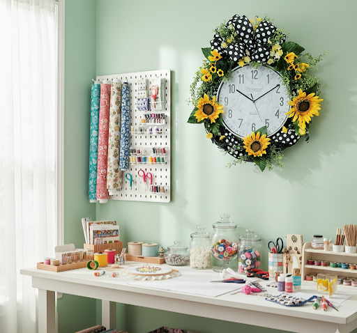 Craft room with a floral clock, pegboard, and various craft supplies on a green wall.