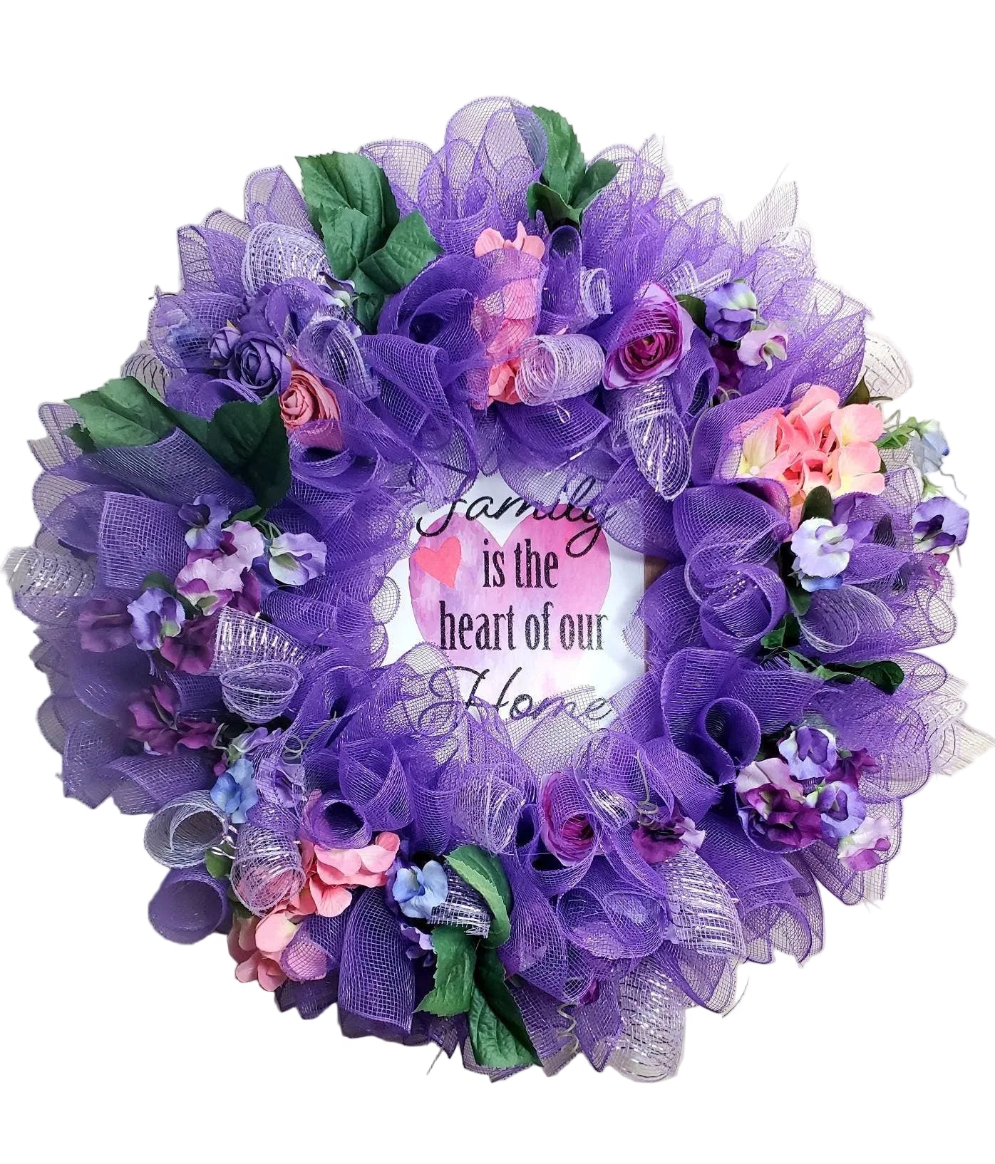 A round purple floral wreath with silk spring flowers and the text 'Family is the heart of our home' on a wire frame.