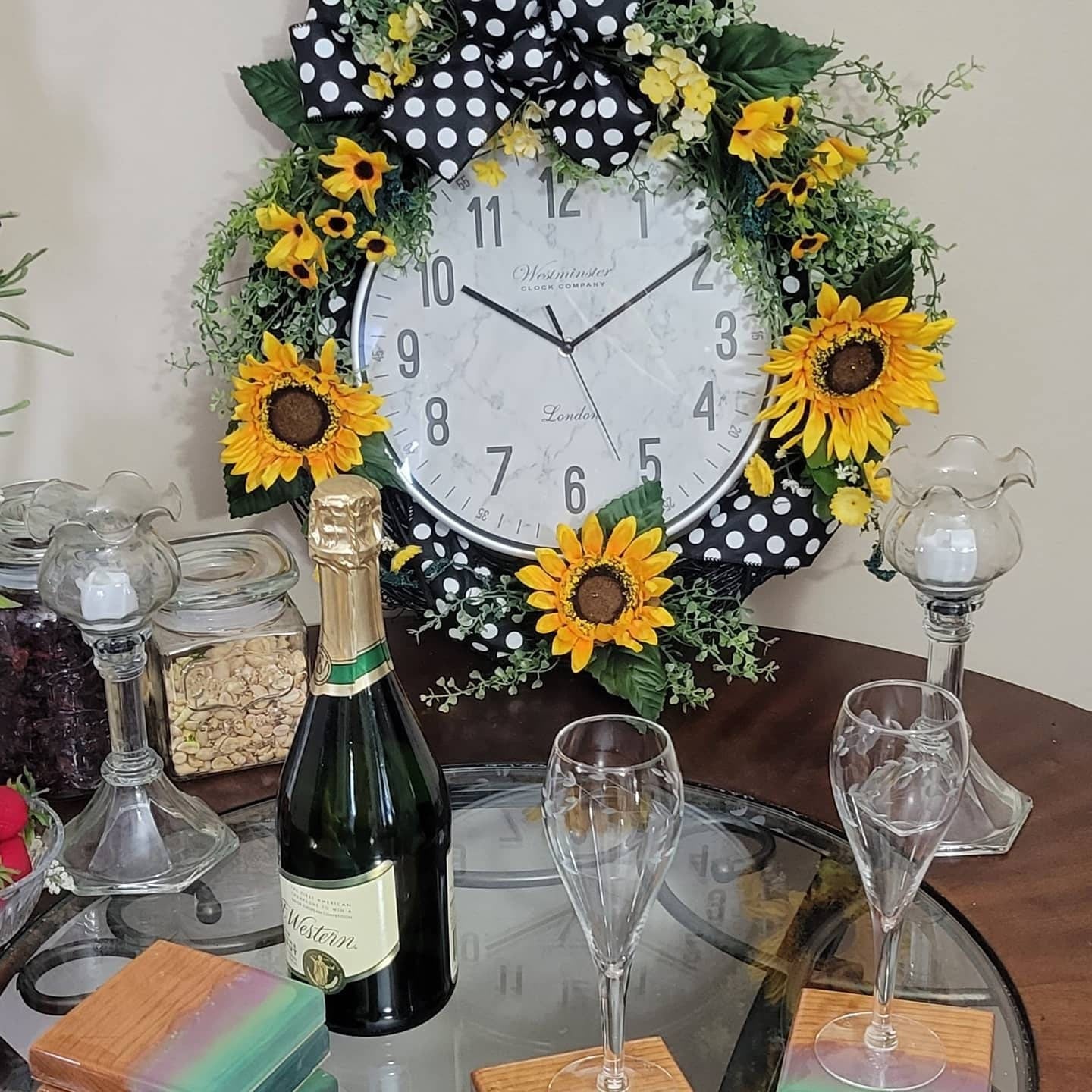 A decorative wreath made with a grapevine clock, artificial flowers, and a handmade bow with polka dots, placed on a table.